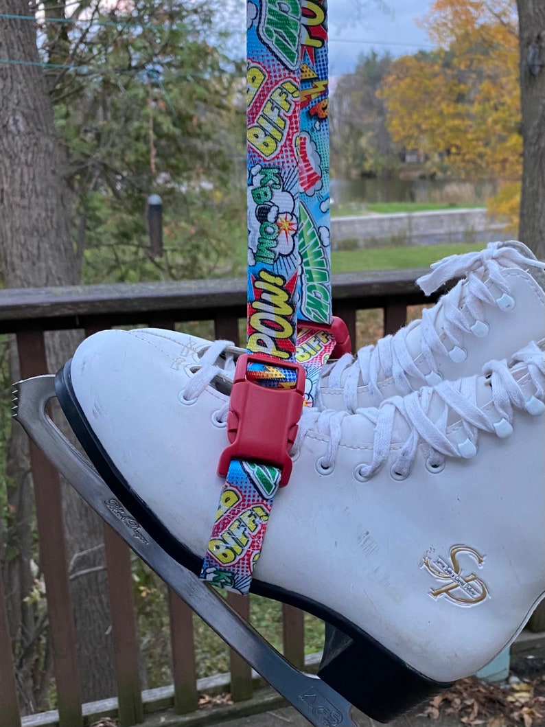 May include: White ice skates with a red and blue comic book print strap attached to the top of the skate. The strap has the words "POW!" and "BIFF!" printed on it.