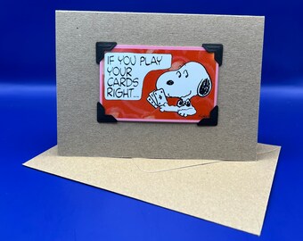 May include: A greeting card featuring a cartoon image of Snoopy holding playing cards. The card has a red background with the text "If you play your cards right..." printed on it.