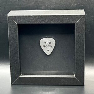 May include: A black framed shadow box with a silver guitar pick inside. The pick has the words "You Rock" engraved on it.
