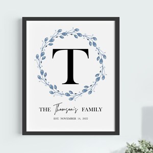 Może przedstawiać: Drukowany projekt sztuki ściennej z niebieską akwarelową girlandą z czarną literą "T" w środku. Tekst "THE Thompson's FAMILY EST. NOVEMBER 14, 2022" znajduje się pod girlandą.