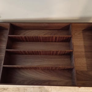 May include: A wooden cutlery tray with four compartments. The tray is made of dark brown wood with a natural grain pattern.