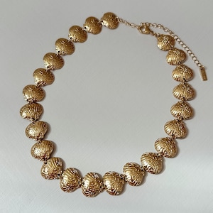 May include: A gold necklace with textured, shell-shaped pendants. The necklace has a delicate chain and clasp, and is displayed against a white background. The jewelry is a statement piece, suitable for special occasions.