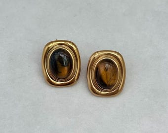 Könnte beinhalten: Ein Paar goldfarbene Ohrringe mit ovalen Tigeraugen-Steinen.