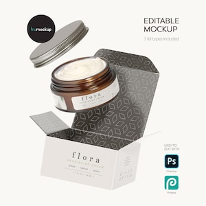 Op de afbeelding: Een bewerkbare mockup van een bruine glazen pot gevuld met witte crème, met een etiket waarop flora NOURISHING CREAM staat, vergezeld van een los metalen deksel en een open witte doos met een donkergrijs geometrisch patroon aan de binnenkant.