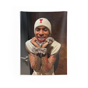 May include: A cream-colored ribbed knit beanie featuring a small red heart logo on the front. The beanie is worn with a sleeveless cream-colored sweater vest, showcasing a large, intricate, silver-toned chain necklace with multiple pendants.