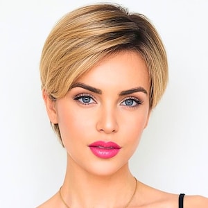 Puede incluir: Una mujer con cabello rubio corto y en capas y ojos azules. Lleva una blusa negra y un collar dorado. Sus labios están pintados de un color rosa brillante. El fondo es blanco liso.