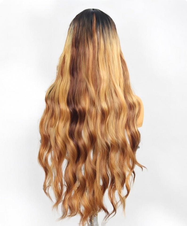 May include: A long, wavy wig featuring a dark brown root color that transitions into a multi-tonal blend of golden blonde and light brown highlights. The hair has a soft, flowing texture with loose waves extending down to the lower back area.