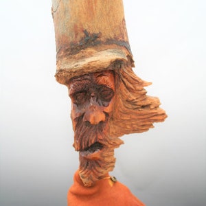 May include: A wooden carving of a man's face with a long beard and a hat. The carving is made from a piece of driftwood and has a rustic, weathered look.