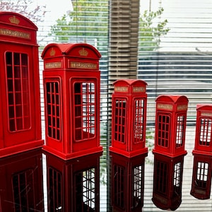 May include: A set of six red miniature telephone boxes, decreasing in size from left to right. Each box has a gold crown and the word "Telephone" on the front.