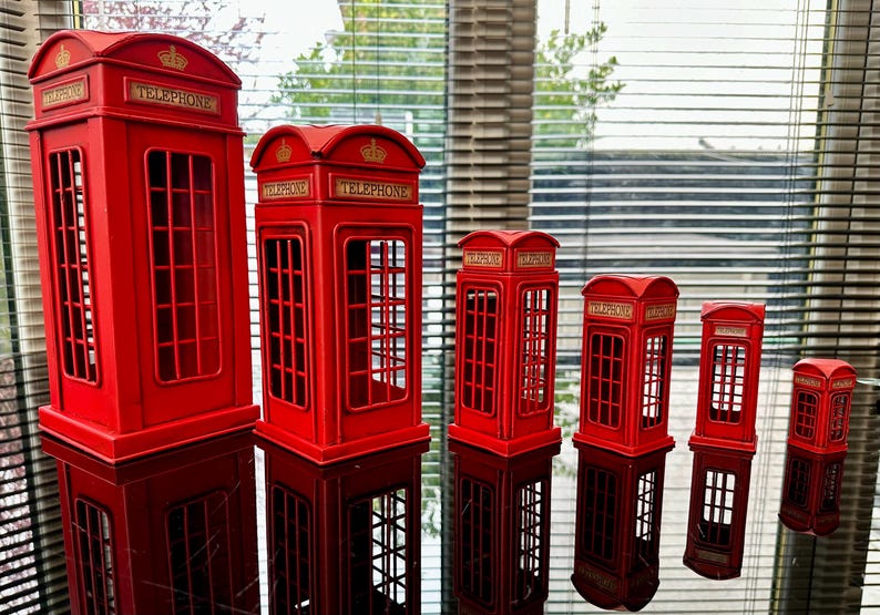 May include: A set of six red miniature telephone boxes, decreasing in size from left to right. Each box has a gold crown and the word "Telephone" on the front.