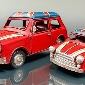 May include: Two red toy cars with white stripes and silver accents. The roofs are blue with a Union Jack design. One car is larger than the other. The cars are miniature replicas of a classic vehicle.