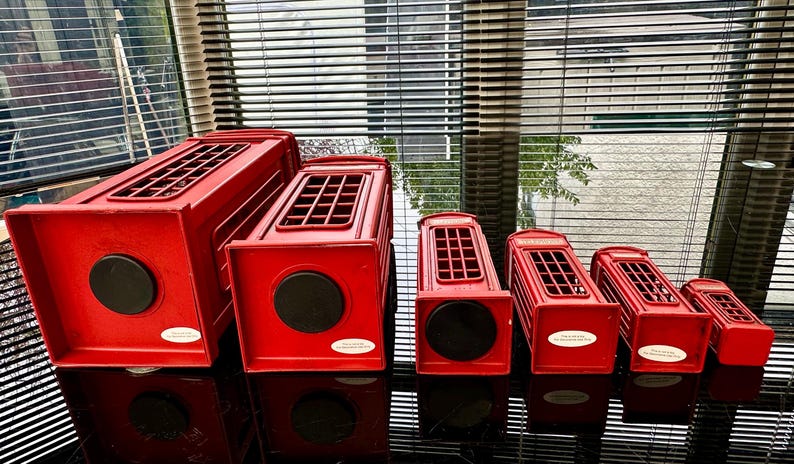May include: A set of six red miniature telephone boxes, decreasing in size from left to right. The boxes are made of metal and have a classic British design.