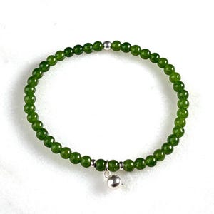 Könnte beinhalten: Ein grünes Perlenarmband mit einem kleinen Silberanhänger. Das Armband besteht aus kleinen, runden, grünen Perlen, die mit silbernen Akzenten aufgefädelt sind. Der Anhänger ist eine kleine, runde Silberperle.