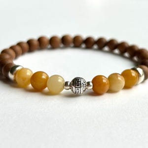 May include: A bracelet with brown wooden beads and yellow-orange gemstone beads. A decorative silver bead with an etched design is also present. This piece of jewellery is a bracelet.