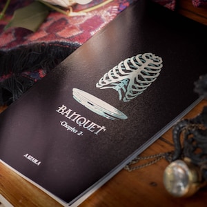 May include: A black book with the title "Banquet" and the subtitle "Chapter 2." The cover features a stylized illustration of a ribcage and a plate.