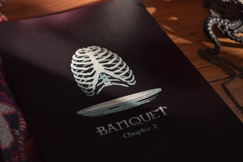 May include: A black book cover with a white ribcage and a plate illustration. The text "BANQUET - Chapter 2." is printed on the cover.
