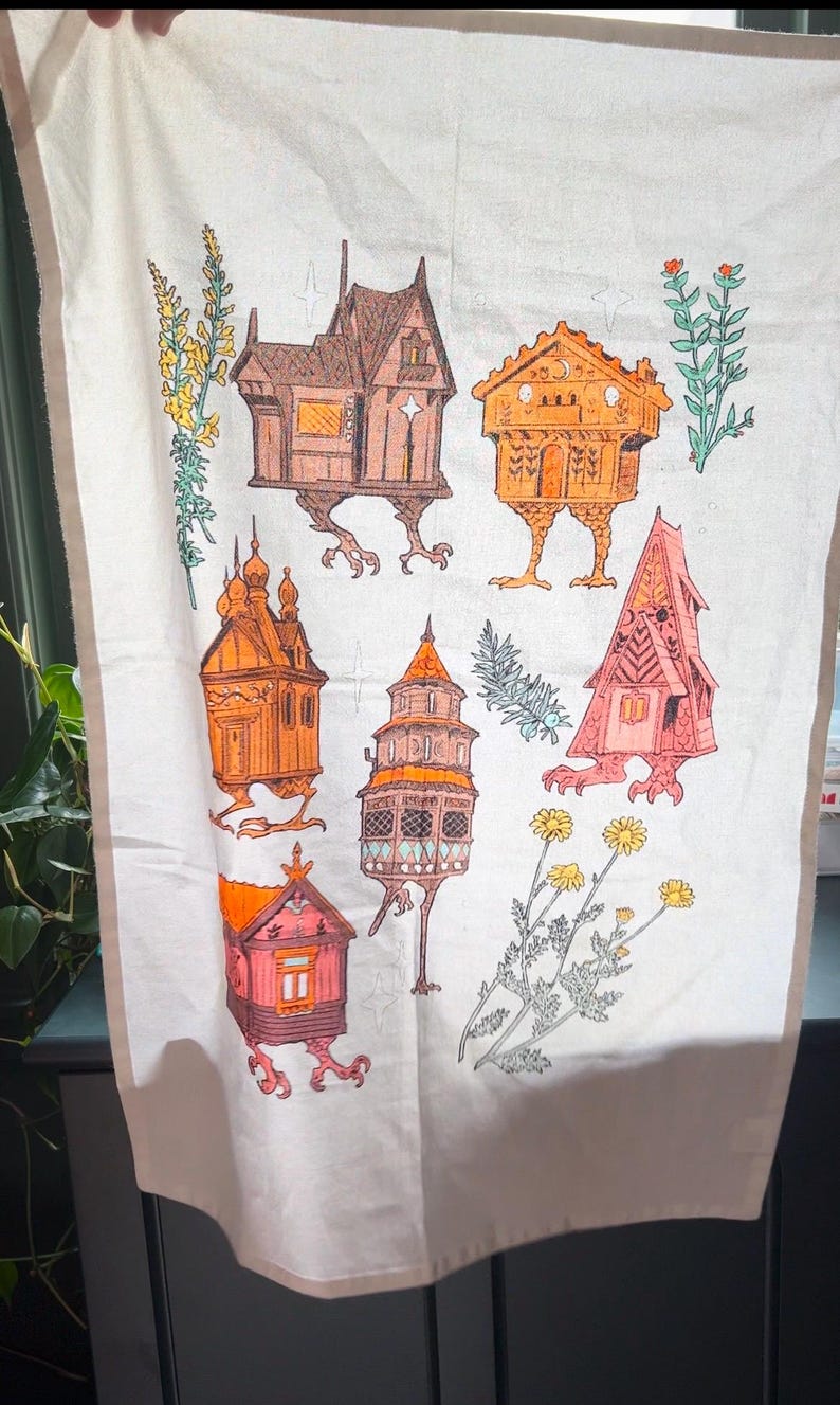 May include: A white tea towel with a colorful illustration of six houses with legs. The houses are in various styles and colors, including red, orange, brown, and pink. The houses are surrounded by green and yellow flowers.