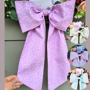 May include: A large, lilac bow with a white polka dot pattern. The bow is tied with a long, flowing tail.