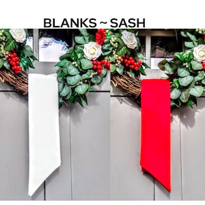 May include: The image features two blank sashes, one white and one red, hanging against a gray background. The sashes are positioned in front of a decorative wreath with white roses, red berries, and green foliage. The text "BLANKS ~ SASH" is at the top.