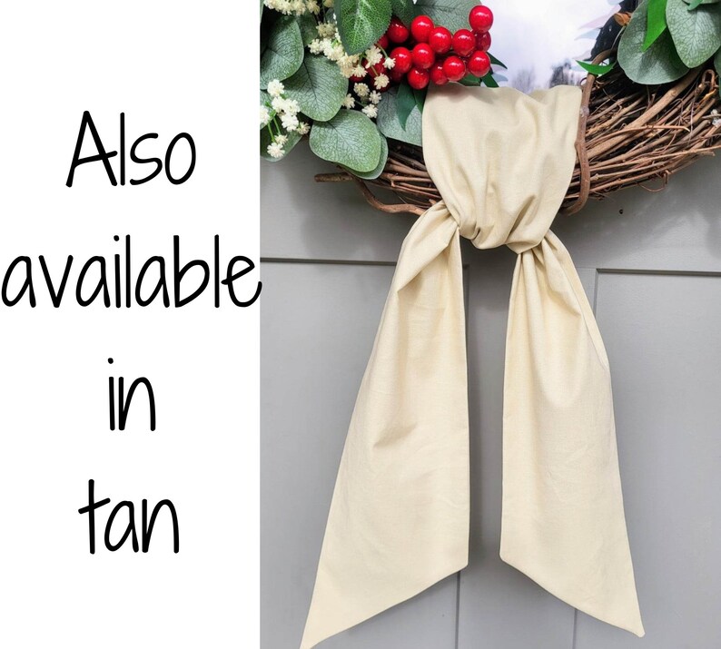 May include: A grapevine wreath adorned with faux greenery, red berries, and a tan fabric bow. The text "Also available in tan" is visible on the left side of the image. This decorative wreath is suitable for seasonal home decor.