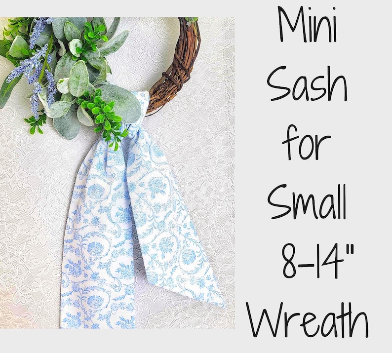 May include: A light blue and white floral patterned fabric sash tied to a small brown twig wreath decorated with green leaves and purple lavender sprigs. The text reads: Mini Sash for Small 8-14" Wreath. The design features a repeating botanical print.