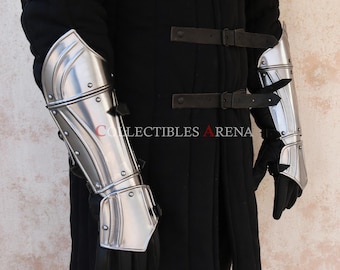 May include: A pair of silver metal arm guards with a decorative design. The guards are worn over black clothing.