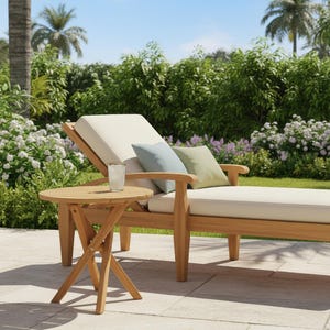 May include: A wooden outdoor chaise lounge with a cream-colored cushion and two pillows, one blue and one green. A small, round wooden side table is next to the lounge, with a glass of water on top. The scene is set outdoors with lush greenery and palm trees.