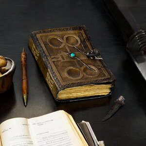 May include: A brown leather-bound journal with a decorative design and a turquoise gemstone. The journal is open to reveal blank pages.