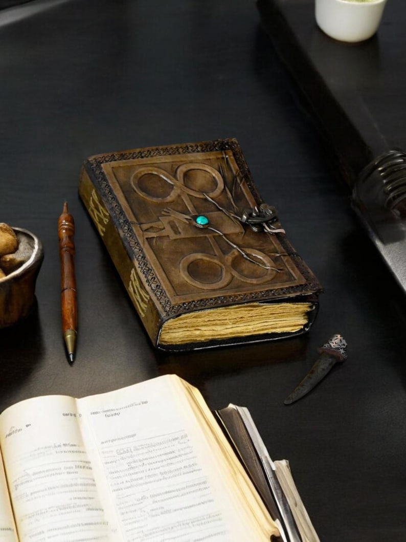 May include: A brown leather-bound journal with a decorative design and a turquoise gemstone. The journal is open to reveal blank pages.