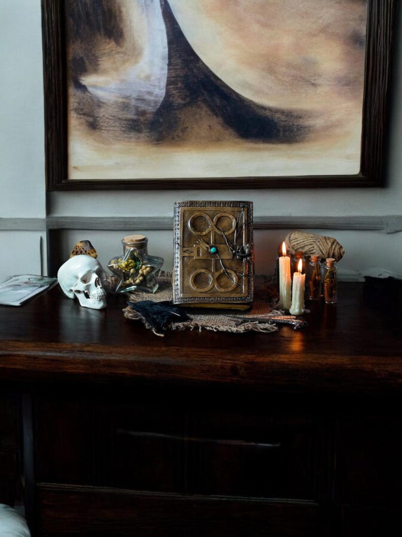 May include: A dark wooden table with a vintage book, a skull, candles, and other decorative items. The book has a leather cover with a metal design and a green gemstone.