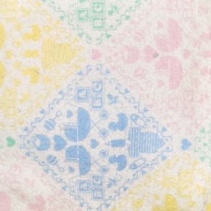 May include: A white baby blanket with a colorful pattern of baby toys and hearts. The pattern is in shades of blue, green, yellow, and pink.