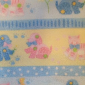 May include: A yellow, blue, and pink fabric with a repeating pattern of animals. The animals are stylized and include a blue elephant, a pink elephant, a blue dog, a pink dog, and a pink cat. The fabric has a striped and dotted pattern.