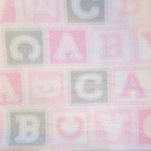 May include: A white fabric with a pink and gray pattern of letters in blocks. The letters are A, B, C, and V.