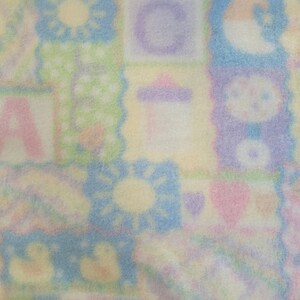 May include: A colorful fabric with a patchwork design featuring letters, hearts, and other shapes. The fabric is made of a soft, fuzzy material and is perfect for baby blankets, quilts, or other craft projects.