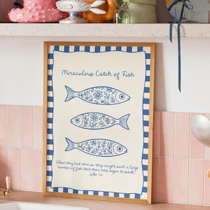 Può includere: Una stampa incorniciata con il testo "Miraculous Catch of Fish" e tre illustrazioni di pesci blu con dettagli floreali. La stampa include un versetto biblico ed è ambientata su uno sfondo crema con un bordo blu.