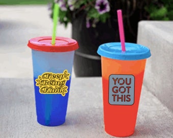 May include: Two colorful reusable tumblers with lids and straws. The tumbler on the left has a blue and red ombre design with the text "Keep Being Kind" in yellow. The tumbler on the right has a red and orange ombre design with the text "You Got This" in white.