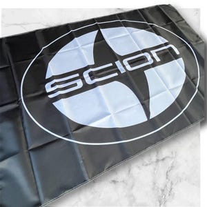 May include: Black and white flag with the Scion logo. The logo is a white circle with a black star inside. The word "SCION" is written in white letters across the star.