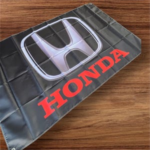 May include: A black flag with a silver Honda logo and the word "HONDA" in red letters.