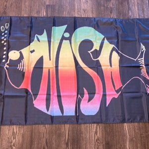 May include: Black flag with the word "WISH" in a colorful, rainbow-gradient font, shaped like a fish. The flag has grommets in the corners for hanging.