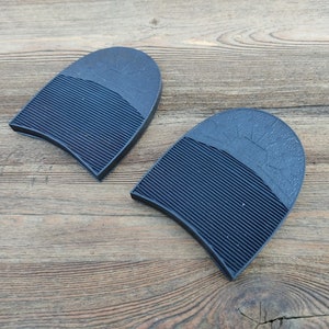 Peut inclure: Deux protections de talon en caoutchouc noir avec une surface texturée. Les protections sont conçues pour être fixées au bas du talon d'une chaussure.