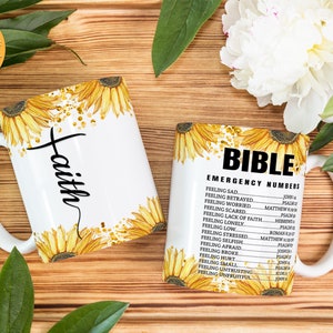 May include: Two white ceramic mugs with sunflower designs. One mug says "faith" and the other says "Bible Emergency Numbers" with a list of Bible verses for different feelings.