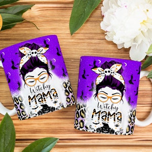Peut inclure: Deux tasses en c&eacute;ramique blanche avec des motifs violets et noirs. Les tasses pr&eacute;sentent une illustration de dessin anim&eacute; d'une femme avec un chignon d&eacute;sordonn&eacute;, des lunettes et un chapeau de sorci&egrave;re. Le texte "Witchy Mama" est imprim&eacute; sur les tasses.