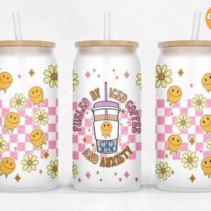May include: White tumbler with a pink and white checkered background. The tumbler has a straw and a wooden lid. The tumbler has a graphic of a cup of iced coffee with the text "Fueled by Iced Coffee and Anxiety". The tumbler is decorated with yellow daisies and smiley faces.
