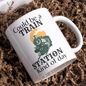 May include: White ceramic mug with a black and green illustration of a train engine with the text "Could be a TRAIN STATION kind of day".
