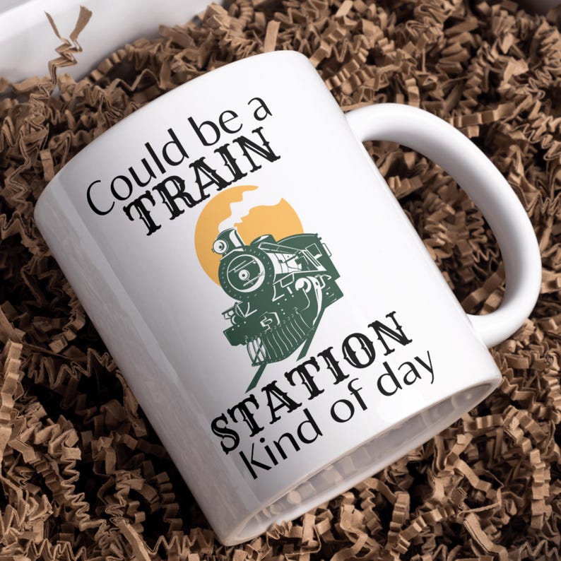May include: White ceramic mug with a black and green illustration of a train engine with the text "Could be a TRAIN STATION kind of day".
