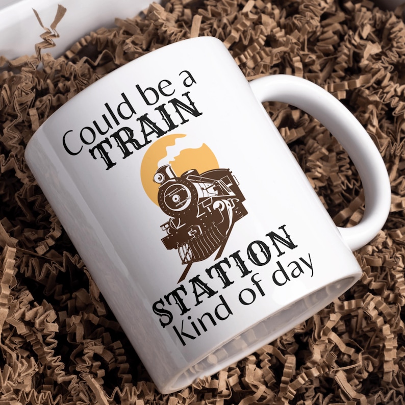 May include: White ceramic mug with a black and brown illustration of a train engine and the text "Could be a TRAIN STATION kind of day".
