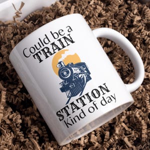 May include: White ceramic mug with a black and blue illustration of a train engine with the text "Could be a TRAIN STATION kind of day".