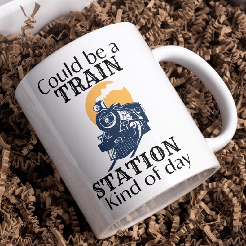 May include: White ceramic mug with a black and blue illustration of a train engine with the text "Could be a TRAIN STATION kind of day".