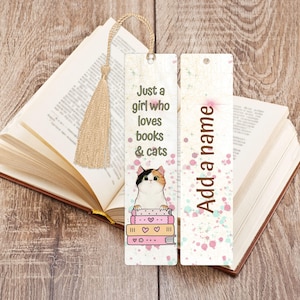 May include: Two rectangular bookmarks with a beige tassel. The left bookmark features a calico cat resting on a stack of pink books with the text Just a girl who loves books & cats. The right bookmark has a white background with pink and blue speckles and the text Add a name.