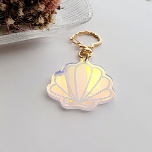 May include: A gold-tone key chain with a white iridescent seashell charm. The seashell has a detailed outline and a pearlescent finish.